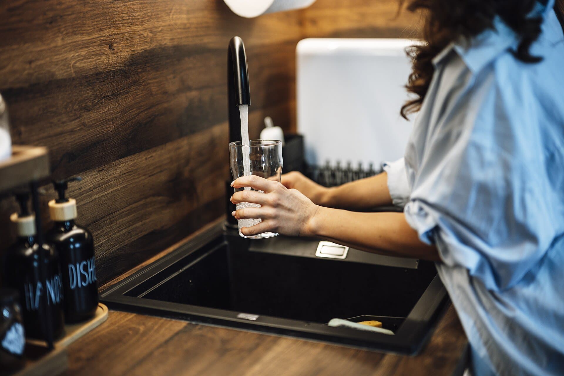 Person filling a glass with water at a kitchen sink
